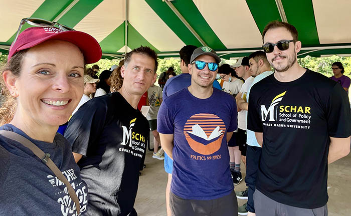 Four people in tee shirts pose for a group selfie.