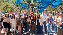 A large group of college students pose in front of a brightly colored mural.