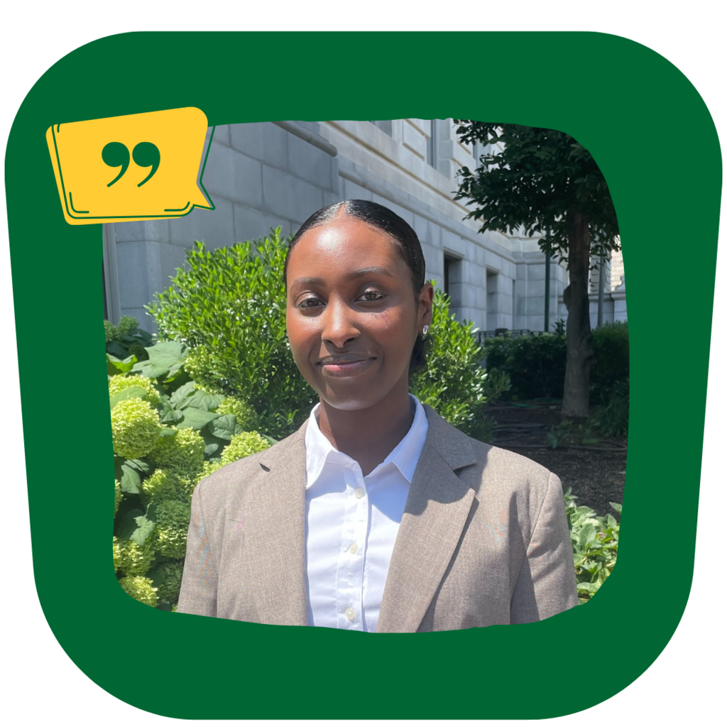 MPP graduate Najma Mohamud, a young woman with brown skin and dark hair wearing a tan suit smiles at the camera